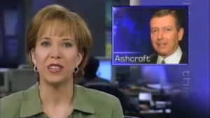 Old image of Loretta on air, wearing a green shirt and apparently in the middle of speaking; on the screen beside her is an image of an older white man's face with the caption "Ashcroft."